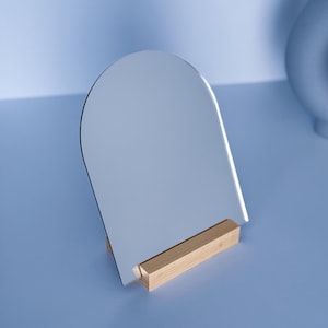 Peut inclure: Un petit miroir arqué avec un pied en bois. Le miroir est argenté et le pied est brun clair.