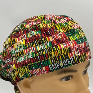 Könnte beinhalten: Eine chirurgische Mütze mit Muster in Schwarz, Rot, Grün und Gelb, auf der die Wörter "Dream", "Lead", "Inspire", "Empower", "Courage", "Truth", "Respect", "Achieve", "Uplift" und "One" aufgedruckt sind.