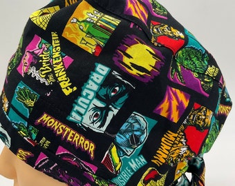 May include: Black scrub hat with a colorful print of classic monster movie characters, including Dracula, Frankenstein, The Mummy, and The Creature from the Black Lagoon. The hat has a tie at the back.