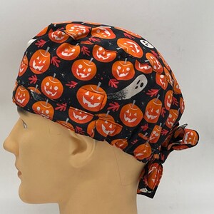 Könnte beinhalten: Schwarze OP-Mütze mit einem Halloween-Kürbis- und Geisterdruck. Die Mütze hat einen Bindfaden an der Rückseite.