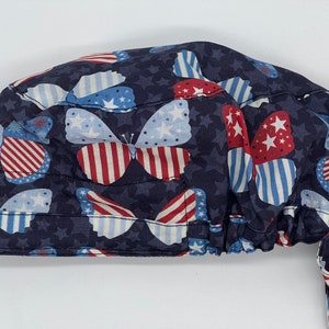 Könnte beinhalten: Eine blaue OP-Mütze mit einem roten, weißen und blauen Schmetterlingsmuster. Die Mütze hat einen Bindegurt an der Rückseite.