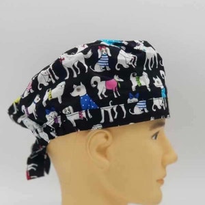 Könnte beinhalten: Schwarze OP-Mütze mit einem bunten Muster von Hunden, die Kleidung tragen. Die Mütze hat einen Bindfaden an der Rückseite.