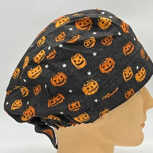 Könnte beinhalten: Schwarze OP-Mütze mit einem Halloween-Kürbis- und Spinnennetz-Muster. Die Mütze hat einen Bindfaden an der Rückseite.
