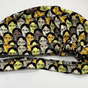 Könnte beinhalten: Eine schwarze OP-Mütze mit einem sich wiederholenden Muster eines Comic-Gesichts mit Brille. Die Mütze hat einen Band, der das gleiche Muster wie die Mütze hat.