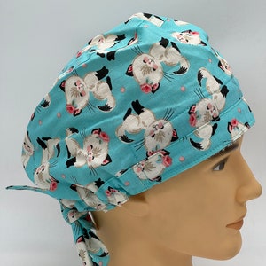 Könnte beinhalten: Eine hellblaue OP-Mütze mit einem weißen Kätzchen-Druck. Die Mütze hat einen Bindfaden an der Rückseite.