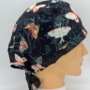 Könnte beinhalten: Schwarze OP-Mütze mit einem bunten Schmetterlings- und Mottenmuster. Die Mütze hat einen Bindegurt an der Rückseite.
