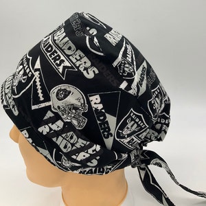 Könnte beinhalten: Schwarze und silberne OP-Mütze mit einem sich wiederholenden Muster des Las Vegas Raiders-Logos. Die Mütze hat einen Bindfaden an der Rückseite.