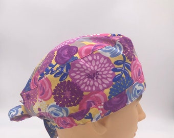 May include: A yellow, pink, purple, and blue floral print scrub hat with a tie at the back.