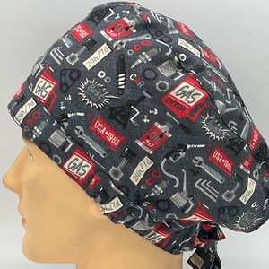 Könnte beinhalten: Eine graue OP-Mütze mit einem roten, weißen und blauen Druck verschiedener Autoteile und Werkzeuge. Der Text "GAS EXTRA" und "USA 1965" ist auf der Mütze sichtbar.