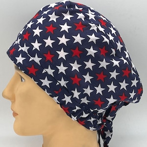 Könnte beinhalten: Eine blaue OP-Mütze mit einem Muster aus weißen und roten Sternen. Die Mütze hat einen Bindegurt an der Rückseite.