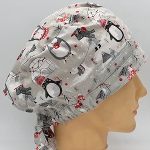 Könnte beinhalten: Eine graue OP-Mütze mit einem winterlichen Druck mit Pinguinen, Eisbären und Iglus. Die Mütze hat eine rot-weiße Schleife.
