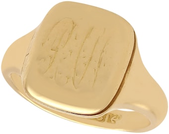 Op de afbeelding: Een gouden zegelring met een vierkante top en een gegraveerd monogram. De ring is gemaakt van 14 karaat goud en heeft een gepolijste afwerking.