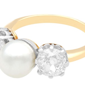 May include: A gold ring with a large pearl and two round diamonds. The diamonds are set in a silver setting.