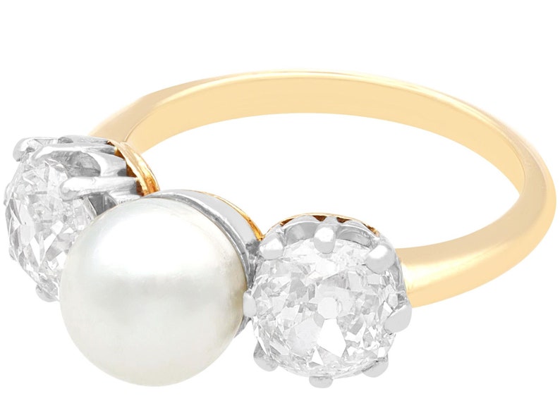 May include: A gold ring with a large pearl and two round diamonds. The diamonds are set in a silver setting.