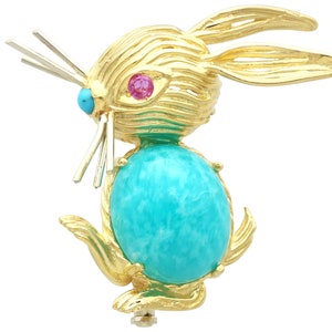 May include: A gold-tone rabbit brooch with a turquoise cabochon stone and red and blue accents.