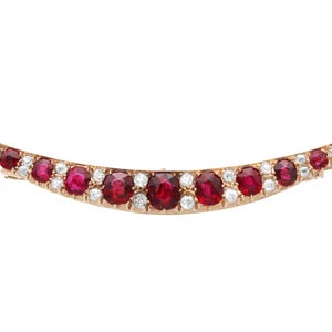 May include: A crescent-shaped brooch with a gold setting. The brooch is adorned with alternating oval-cut rubies and round diamonds. The gemstones are set closely together, creating a sparkling, elegant design. The brooch is a piece of jewelry.