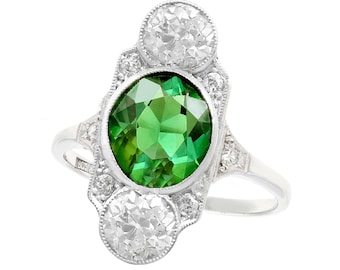 May include: A vintage ring featuring a large green gemstone surrounded by smaller diamonds. The ring is set in platinum and has a delicate, Art Deco design.