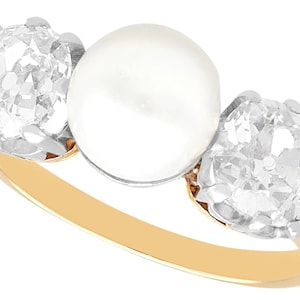 May include: A gold ring with a large white pearl in the center and two smaller diamonds on either side.
