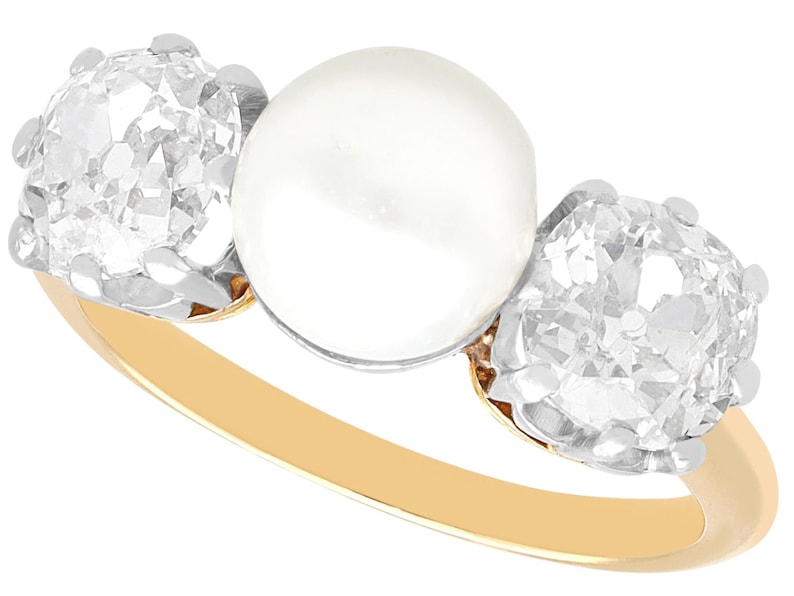 May include: A gold ring with a large white pearl in the center and two smaller diamonds on either side.