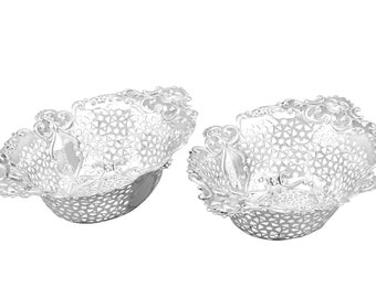 Op de afbeelding: Twee zilveren decoratieve kommen met een ingewikkeld, opengewerkt ontwerp. De kommen zijn ovaalvormig en hebben een delicaat, bloemmotief.