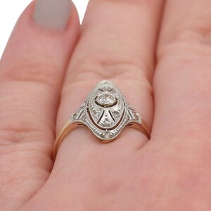 May include: A vintage-style diamond engagement ring with a pointed oval-shaped setting. The ring is made of yellow and white gold and features a central diamond surrounded by smaller diamonds.