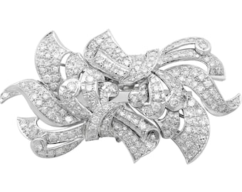 Op de afbeelding: Een zilveren broche met een bloemmotief, bezet met glinsterende diamanten.