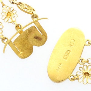 May include: A gold necklace with a delicate chain and floral accents. The necklace has a clasp with a heart-shaped design and a tag with the inscription "800 925 GSH".