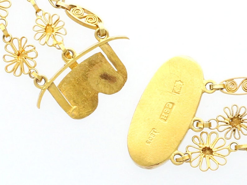 May include: A gold necklace with a delicate chain and floral accents. The necklace has a clasp with a heart-shaped design and a tag with the inscription "800 925 GSH".