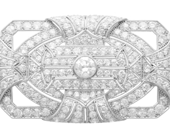 Op de afbeelding: Een zilveren broche met een geometrisch ontwerp, met een grote centrale diamant omringd door kleinere diamanten.