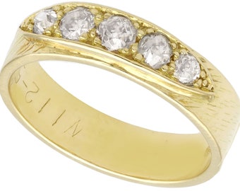 May include: A gold band with five clear round diamonds set in a row. The band is engraved with the text "WII 1-23".