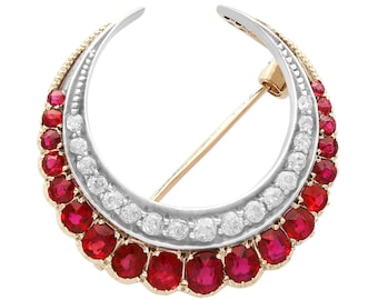 Op de afbeelding: Een halve maanvormige broche met een rij rode robijnen en een rij witte diamanten. De broche is gemaakt van goud en zilver.
