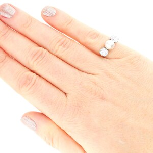 May include: A silver ring with three round white pearls set in a row. The ring is on a person's finger.