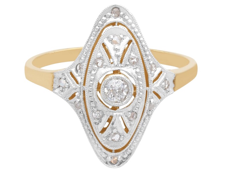 May include: A gold and silver ring with a large, round diamond in the center. The diamond is surrounded by smaller diamonds in a geometric pattern.