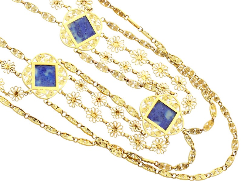 May include: A multi-strand gold necklace with blue stone accents. The necklace features a delicate floral design and square-shaped stones.