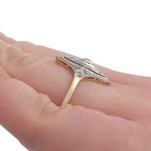 May include: A vintage diamond ring with a geometric design. The ring is set in yellow gold and features a central diamond surrounded by smaller diamonds. The ring is on a finger.
