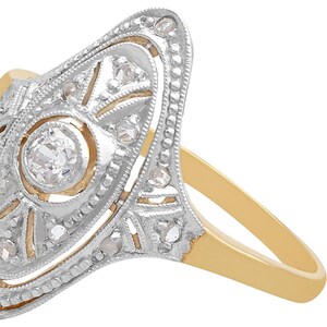 May include: A vintage diamond ring with a delicate, intricate design. The ring features a central round diamond surrounded by smaller diamonds set in a gold band.