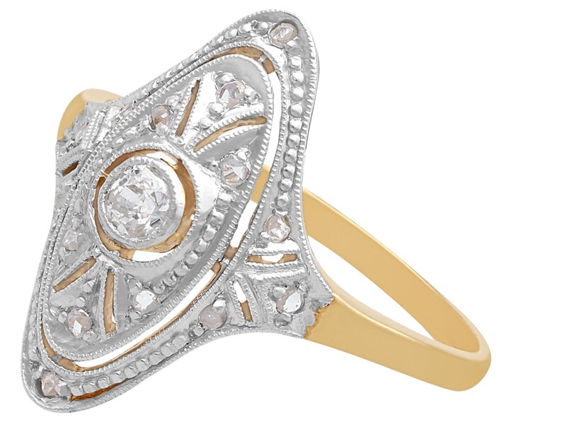 May include: A vintage diamond ring with a delicate, intricate design. The ring features a central round diamond surrounded by smaller diamonds set in a gold band.