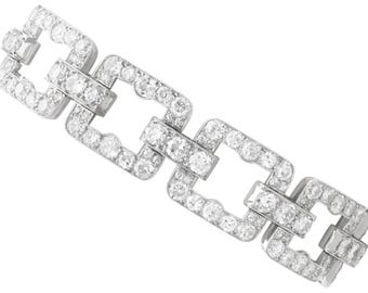 Könnte beinhalten: Ein silbernes Armband mit quadratischen Gliedern, die mit zahlreichen kleinen, runden, klaren Edelsteinen besetzt sind. Die Glieder sind miteinander verbunden und bilden eine durchgehende Kette. Der Hintergrund ist weiß.