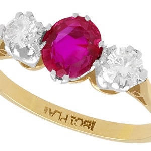 May include: A gold ring with a large oval ruby and two smaller round diamonds. The ring is marked "18CT LA."