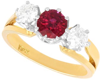 May include: A gold ring with a large red ruby gemstone and two smaller white diamond gemstones. The ring is marked "18ct" on the inside band.