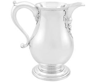 Op de afbeelding: Een zilveren kan met een rond lichaam en een uitlopende basis. De kan heeft een gebogen handvat en een tuit. De kan is versierd met een bloemmotief.