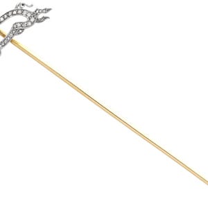 Puede incluir: Un prendedor de estilo vintage con un diseño de animal estilizado. La cabeza del prendedor está adornada con pequeñas piedras brillantes y un ojo de rubí. El prendedor tiene un largo vástago dorado, perfecto para asegurar a prendas o accesorios.