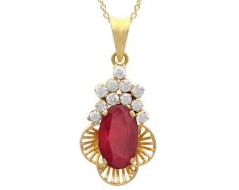 Op de afbeelding: Een gouden ketting met een hanger met een grote ovale robijn, omringd door kleinere witte edelstenen. De hanger is gezet in een delicaat filigraan ontwerp van goud.