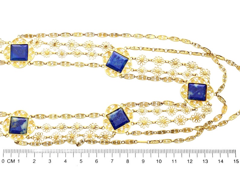 May include: A gold chain necklace with five strands featuring a delicate floral design and square lapis lazuli stones. The necklace is measured on a ruler in inches.