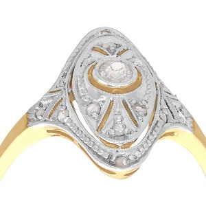 May include: A gold and silver ring with a large, round, clear diamond in the center. The ring is set with smaller diamonds around the center stone and on the band.