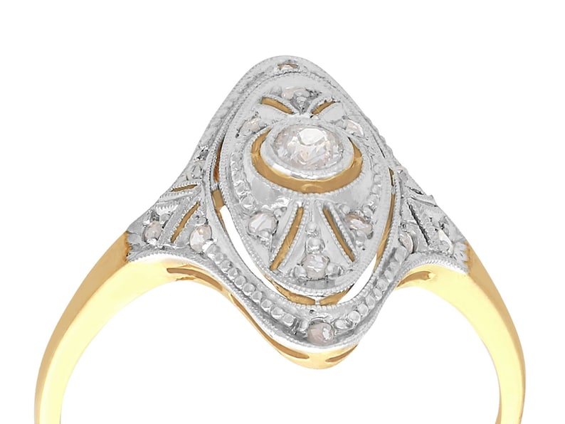May include: A gold and silver ring with a large, round, clear diamond in the center. The ring is set with smaller diamonds around the center stone and on the band.