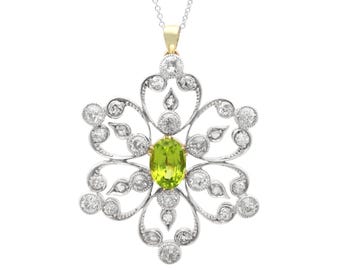 Op de afbeelding: Een hangerketting met een bloemmotief. De hanger heeft een centrale ovaal geslepen, lichtgroene edelsteen, omgeven door een zilverkleurig metalen frame met heldere, ronde edelstenen. De ketting is zilverkleurig.