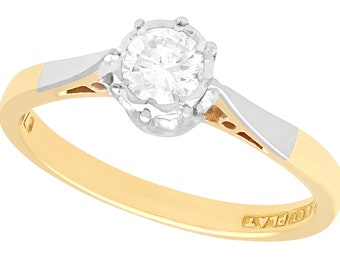May include: A gold and white gold engagement ring with a single round diamond set in a six-prong setting. The ring is marked "18ct PLAT".