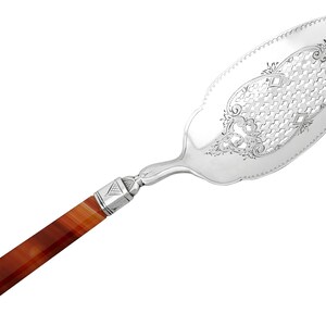 May include: A silver cake server with an ornate, pierced design and a red agate handle.