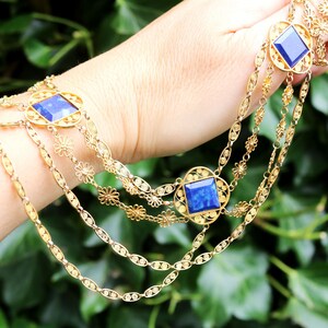 May include: A gold chain necklace with three strands and blue gemstone accents. The necklace features a delicate floral design.